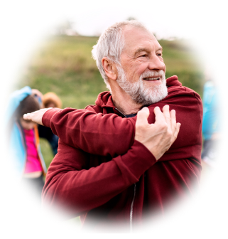An older man stretches his arm while smiling outside.