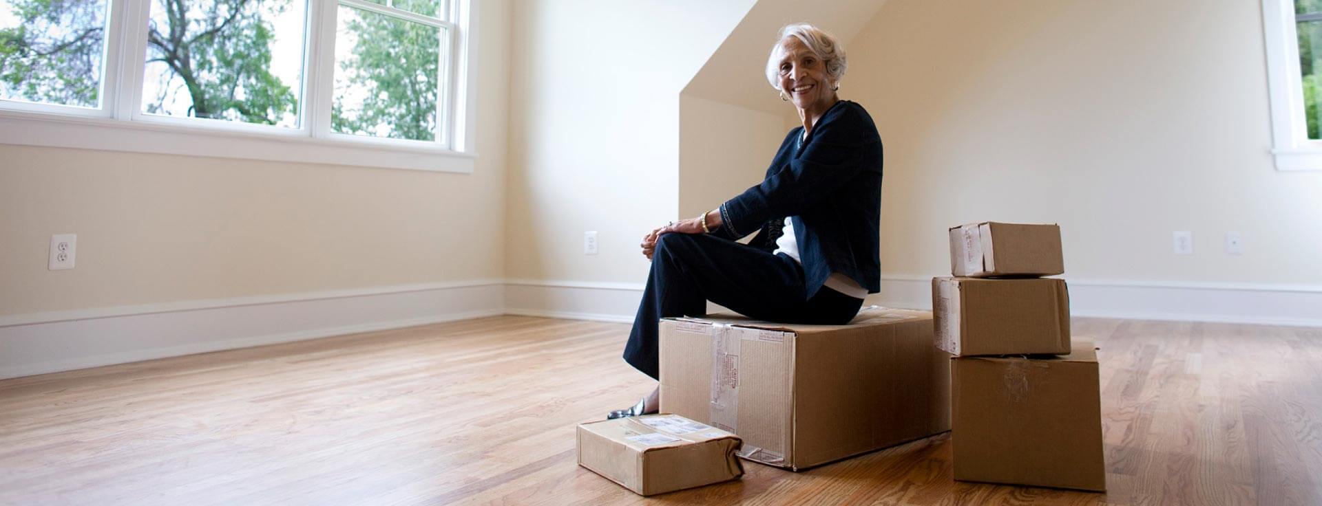 woman smiling as she sits on top of cardboard moving boxes