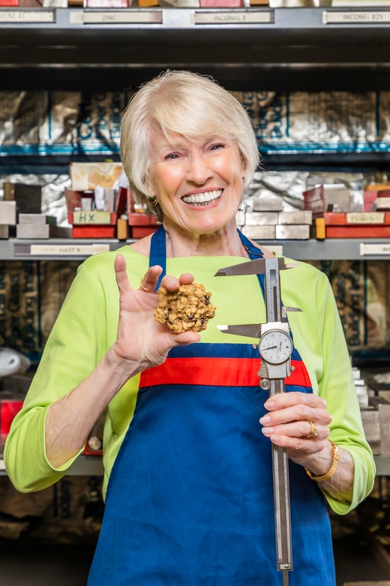 Carolyn wearing an apron while holding a cookie and a measuring tool