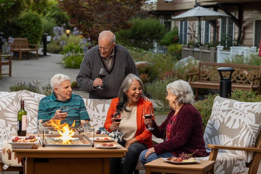 Four seniors drinking wine and chatting on an outdoor patio at The Terraces at Los Altos