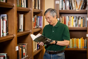 Senior man looking at book in the library at The Terraces at Los Altos