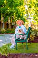 Senior woman wearing a sun hat while sitting on an outdoor bench and holding a small dog