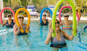 seniors holding pool noodles while water excercising