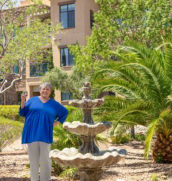 Senior woman holding a glass of wine next to a fountain on the grounds of Las Ventanas at Summerlin