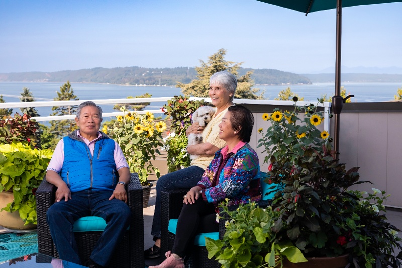 People sitting on a balcony surrounded by garden flowers and water views.