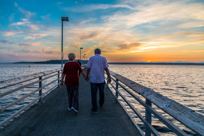 A couple holds hands as they walk along a boardwalk at sunset