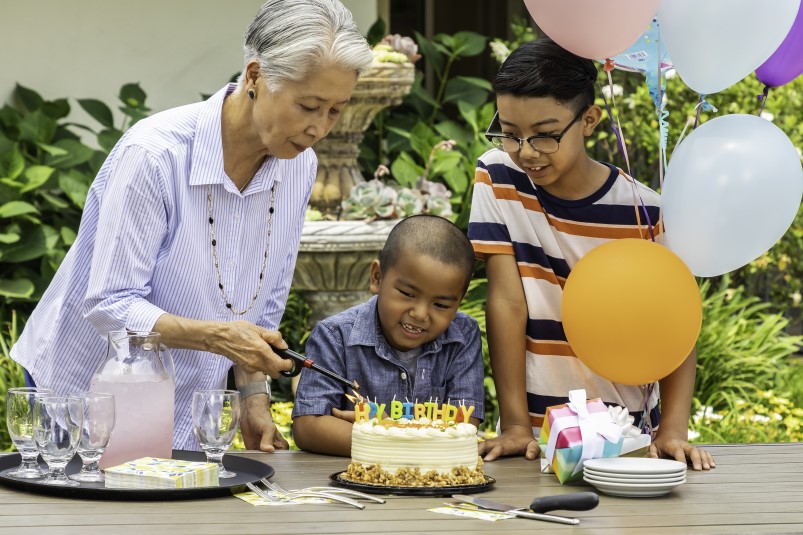 Woman cutting a birthday cake with her grandsons