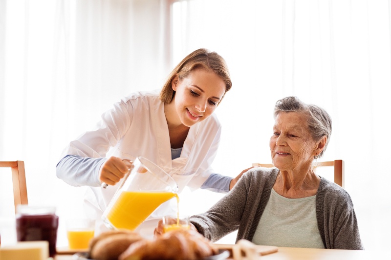 A nurse pouring a pitcher of orange juice for a senior resident in an assisted living community