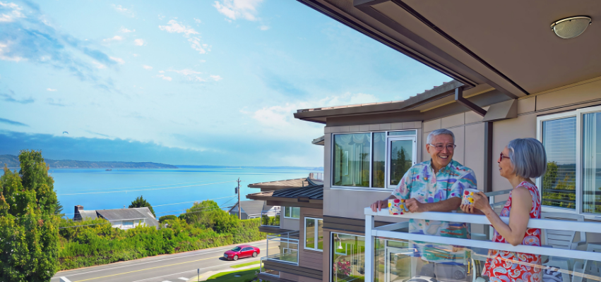 Residents of Judson Park, a HumanGood community, gather together in a bright common area, smiling and spending time with one another in a welcoming, comfortable setting.