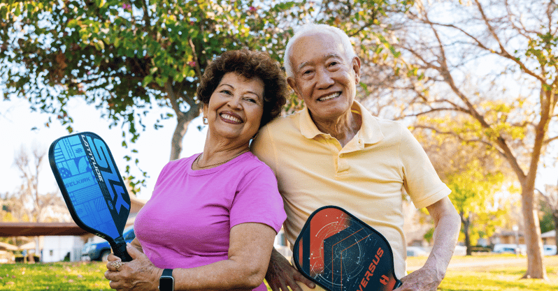 Residents smiling and holding pickleball paddles in a sunny park