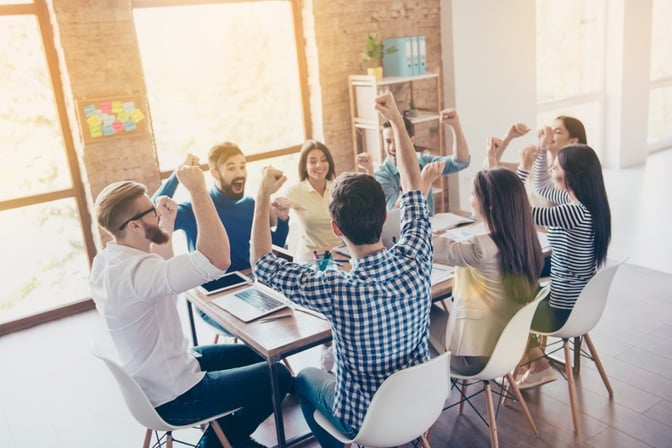 Millennial employees sit around a table and cheer. 