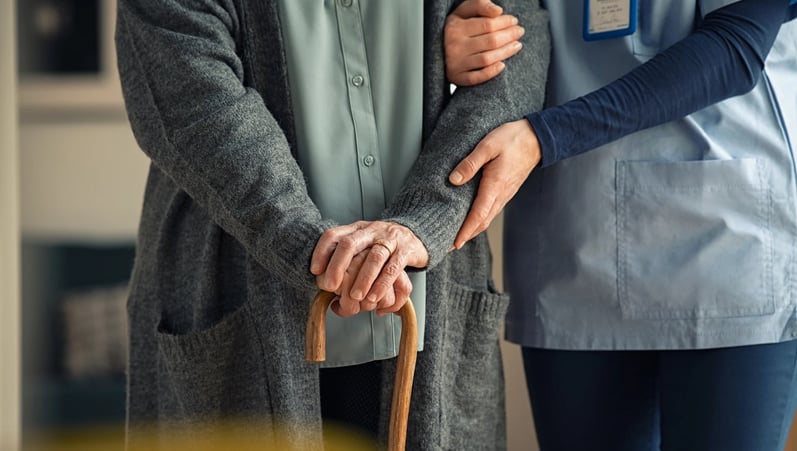 An individual with a cane is being helped by a nurse.