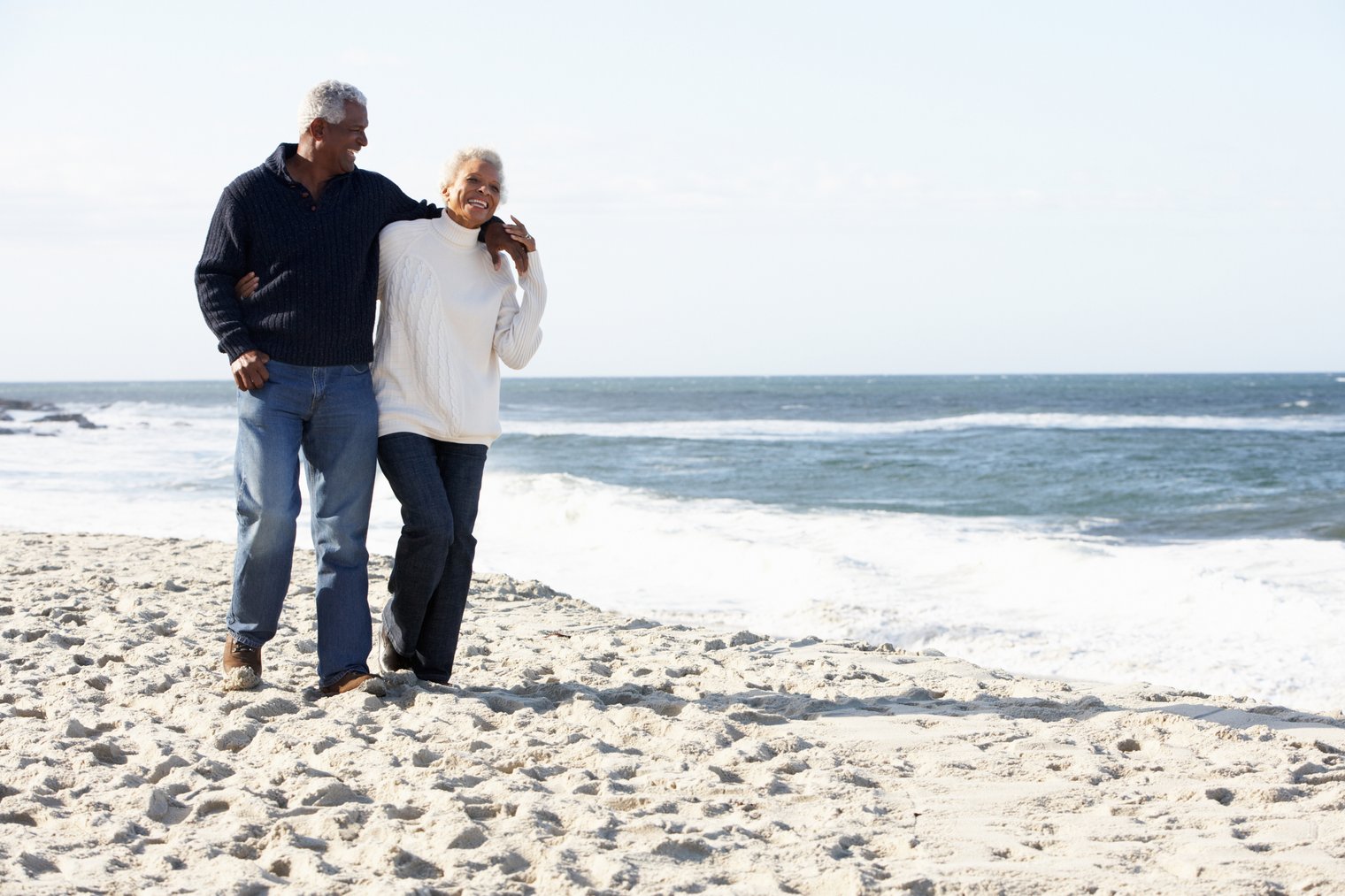 happy retired couple walking together along the beach in California