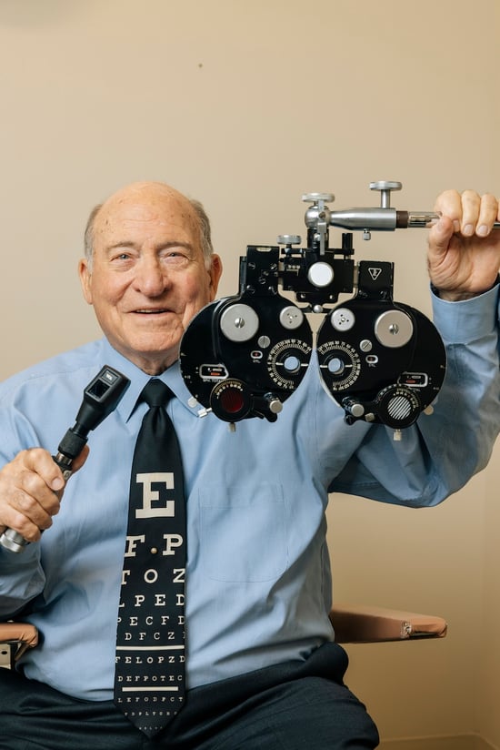 An older man smiling while holding a phoropter