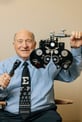An older man smiling while holding a phoropter