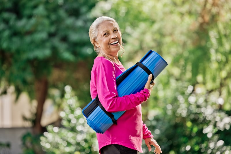 woman smiling with yoga mat outside