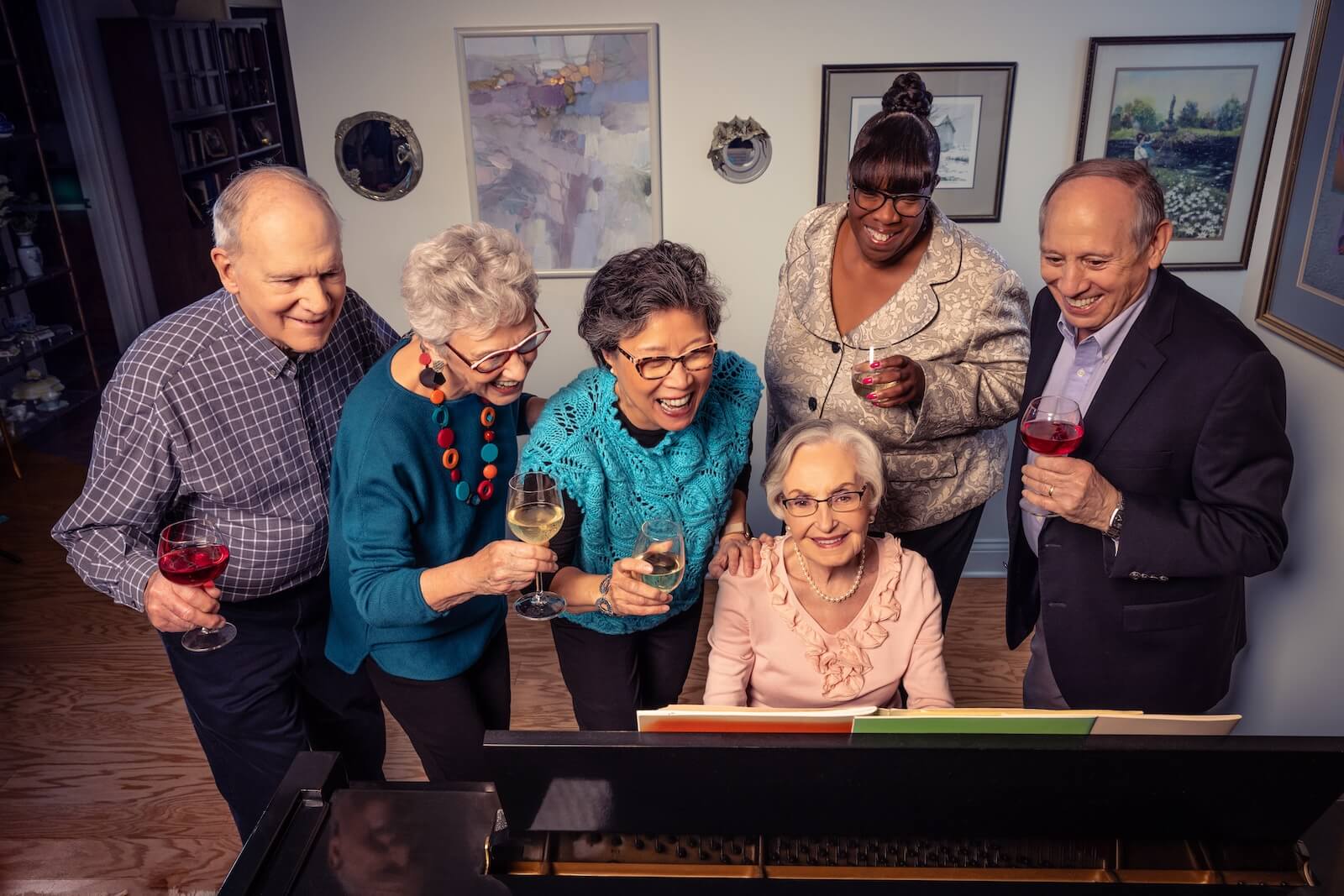 Six seniors with drinks gathered around the piano