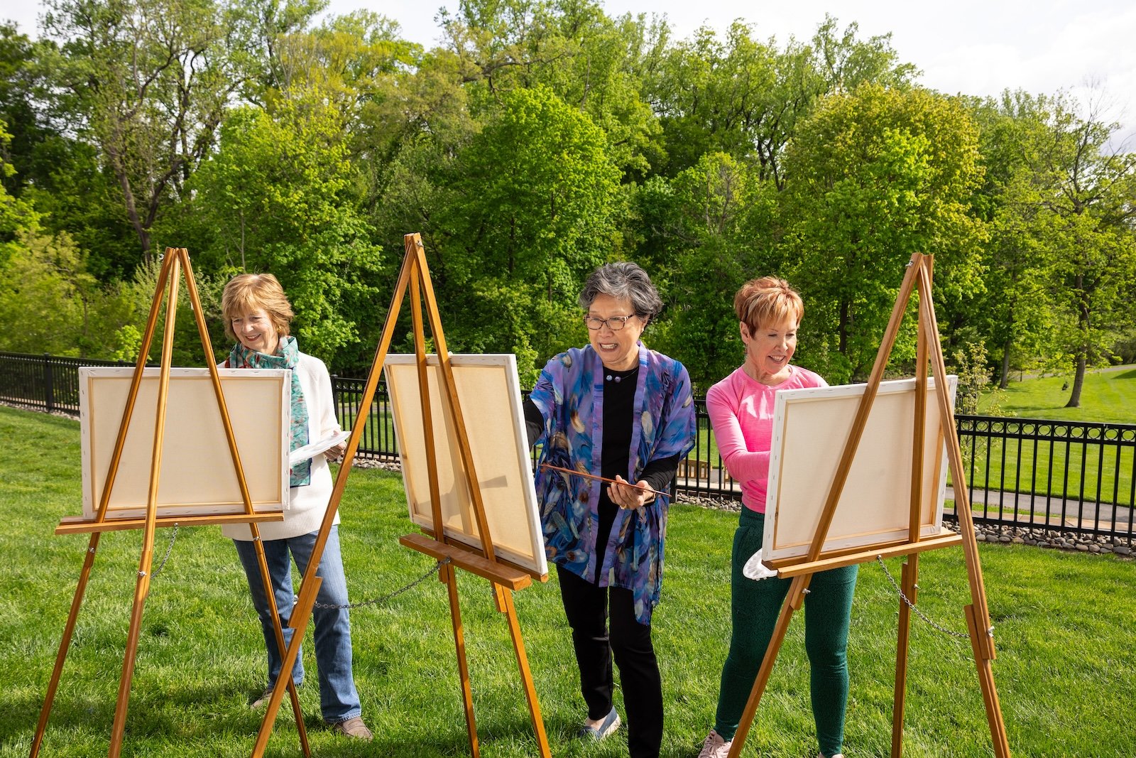 group of three women painting on easels outside