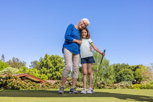Senior woman hugging a young girl who is holding a putter
