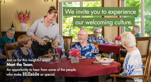 Residents having a meal together in a dining room, served by a smiling woman.