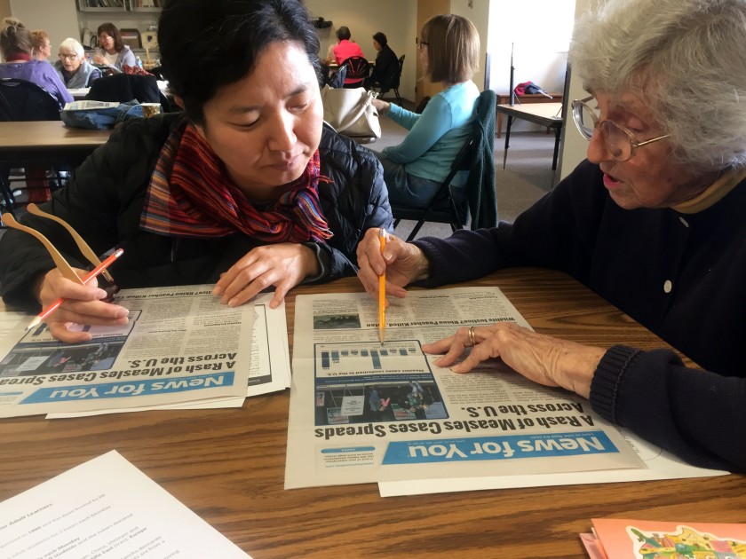 A senior woman shows another woman a graph in the newspaper.