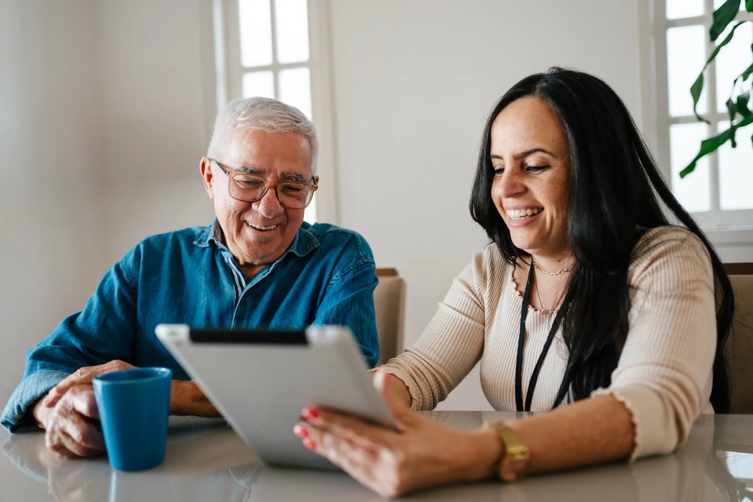 A smiling woman shows a tablet to a man in a cozy room