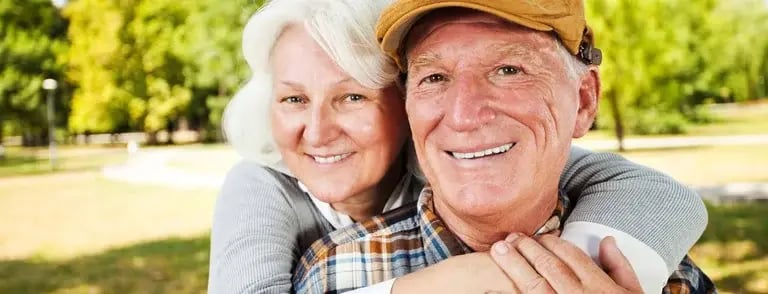 Couple embracing in a sunny park, smiling with warmth and joy.