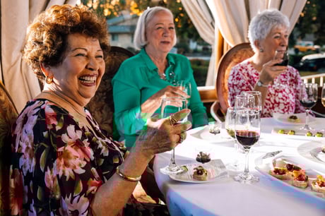 Three women seated at a table outdoors, holding glasses and enjoying appetizers.
