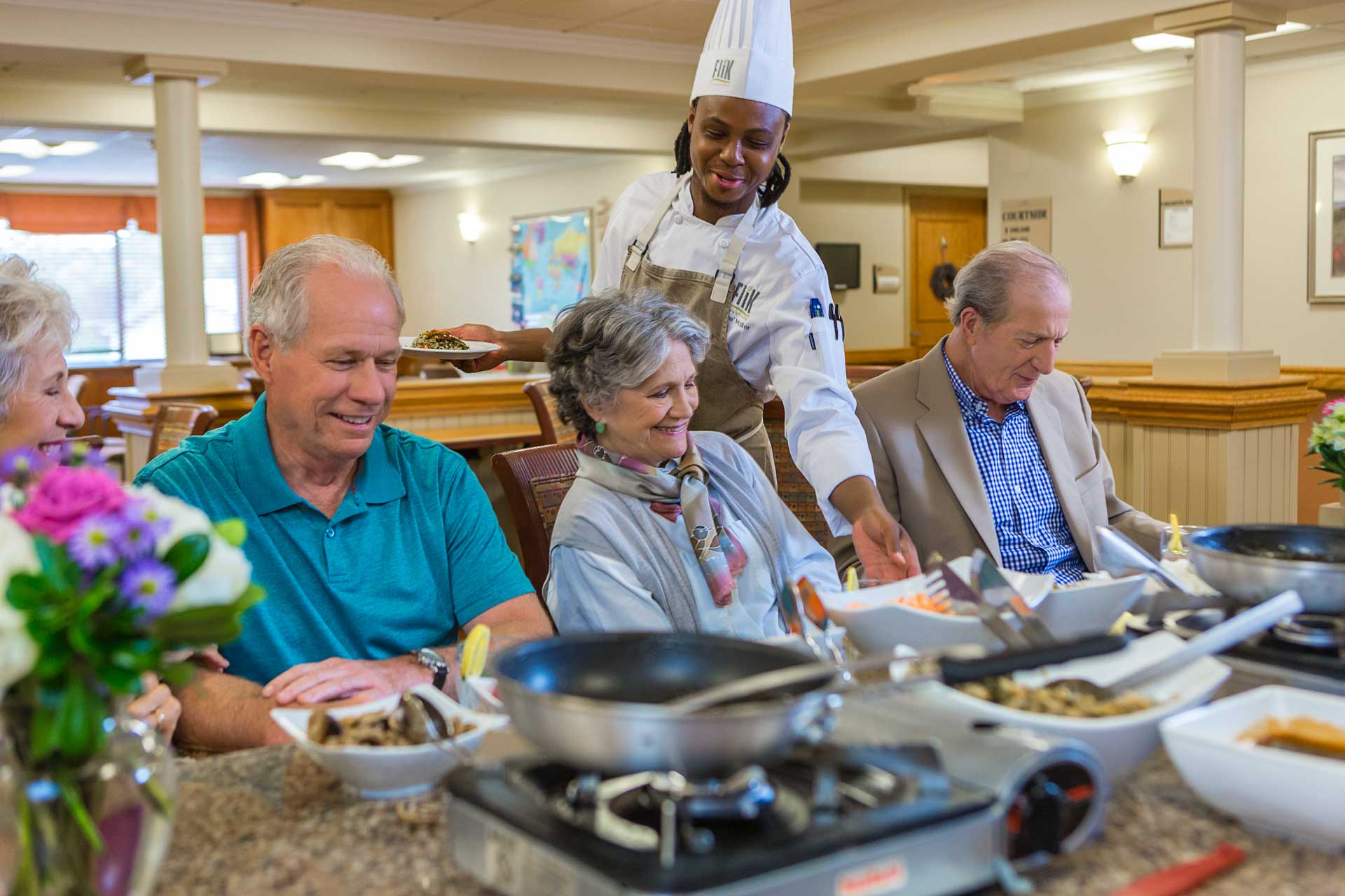 Chef serving meal to two senior men and a senior woman in the Spring Mill Pointe dining room