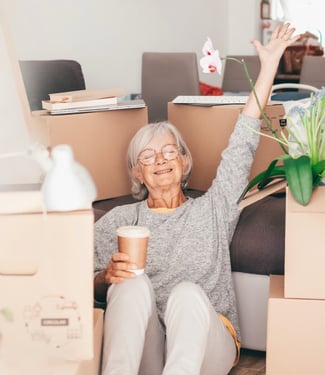 Resident relaxing among moving boxes, holding a coffee cup with one arm raised.