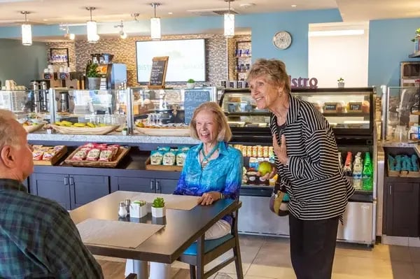 Older adults chatting and laughing in a café-style dining area.