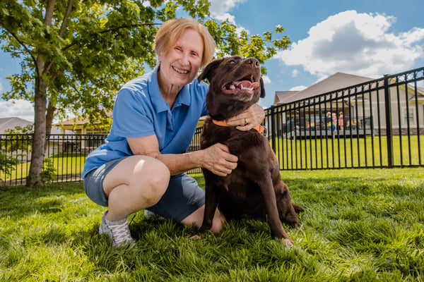 Senior woman kneeling with her arm around a dog