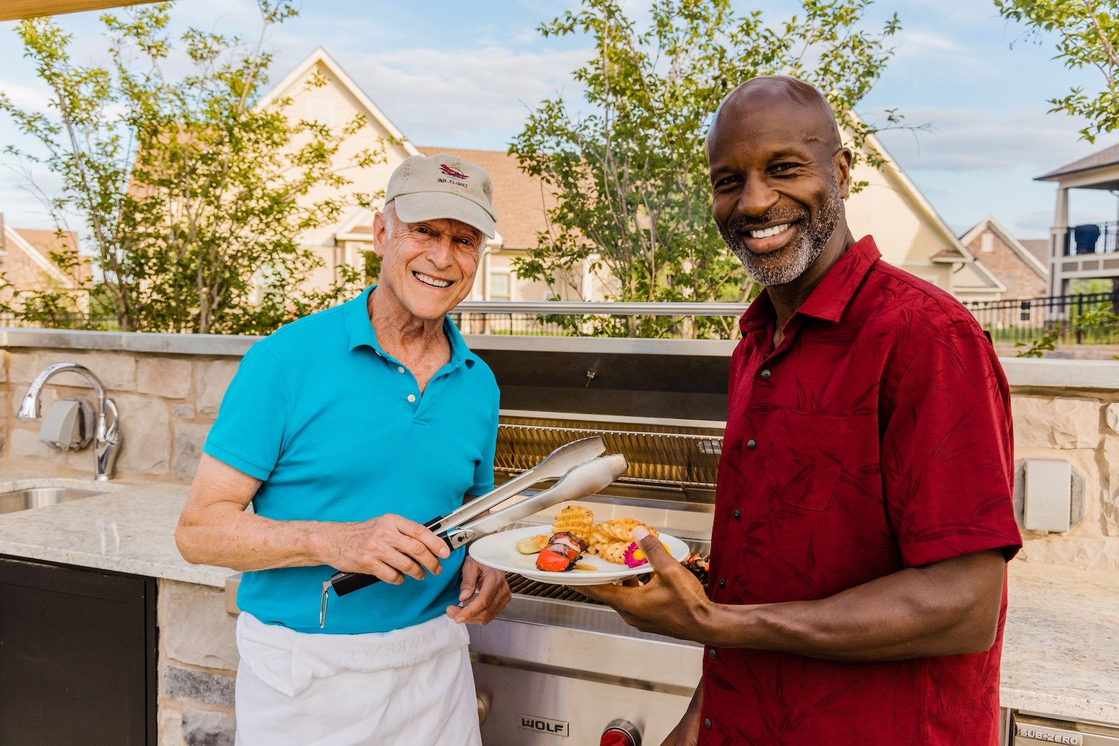 two men smiling and grilling outside