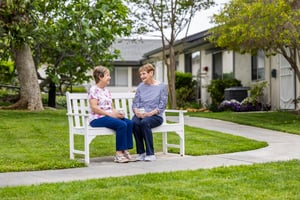 Two woman sitting and talking on a white bench