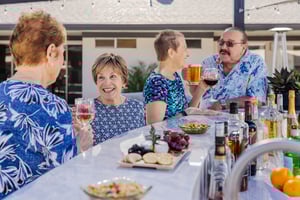Four happy seniors enjoying drinks and snacks at an outdoor bar