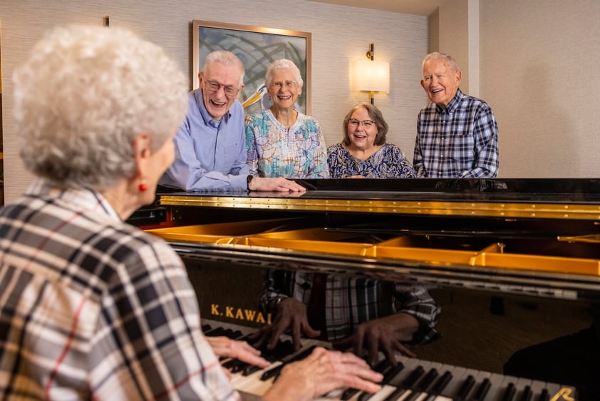 Senior woman playing the piano while four other seniors enjoying the performance