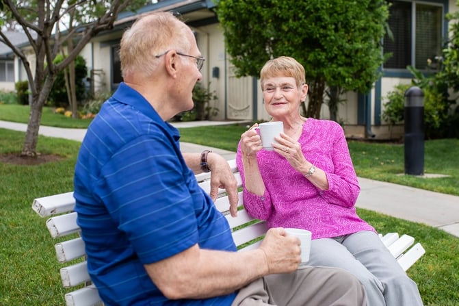Two seniors having coffee outside on a bench
