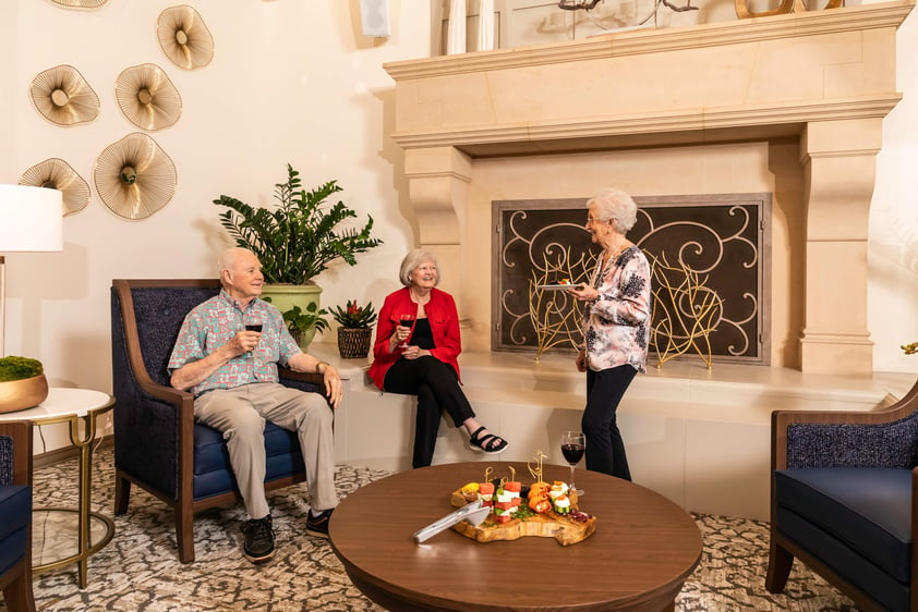 Three seniors enjoying a glass of wine and snacks around a fireplace