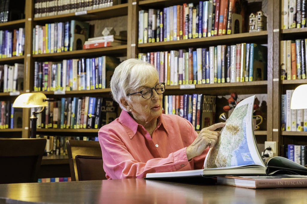 Senior woman in the library pointing at a spot on a map in a book 