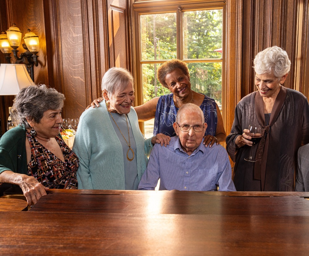 Seniors gather around the piano for a joyful sing-along at The Mansion at Rosemont