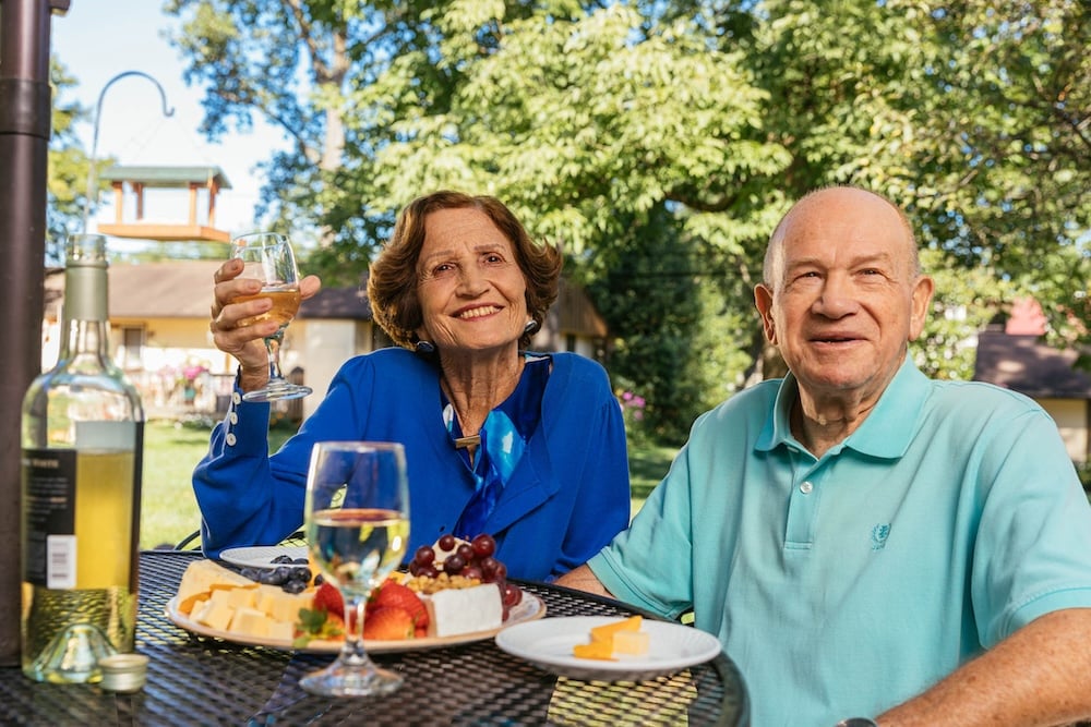 A senior woman and man enjoying wine and cheese board outside