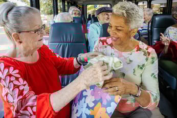  Two smiling residents on a Rosewood community bus, looking at purchases from a patterned shopping bag.