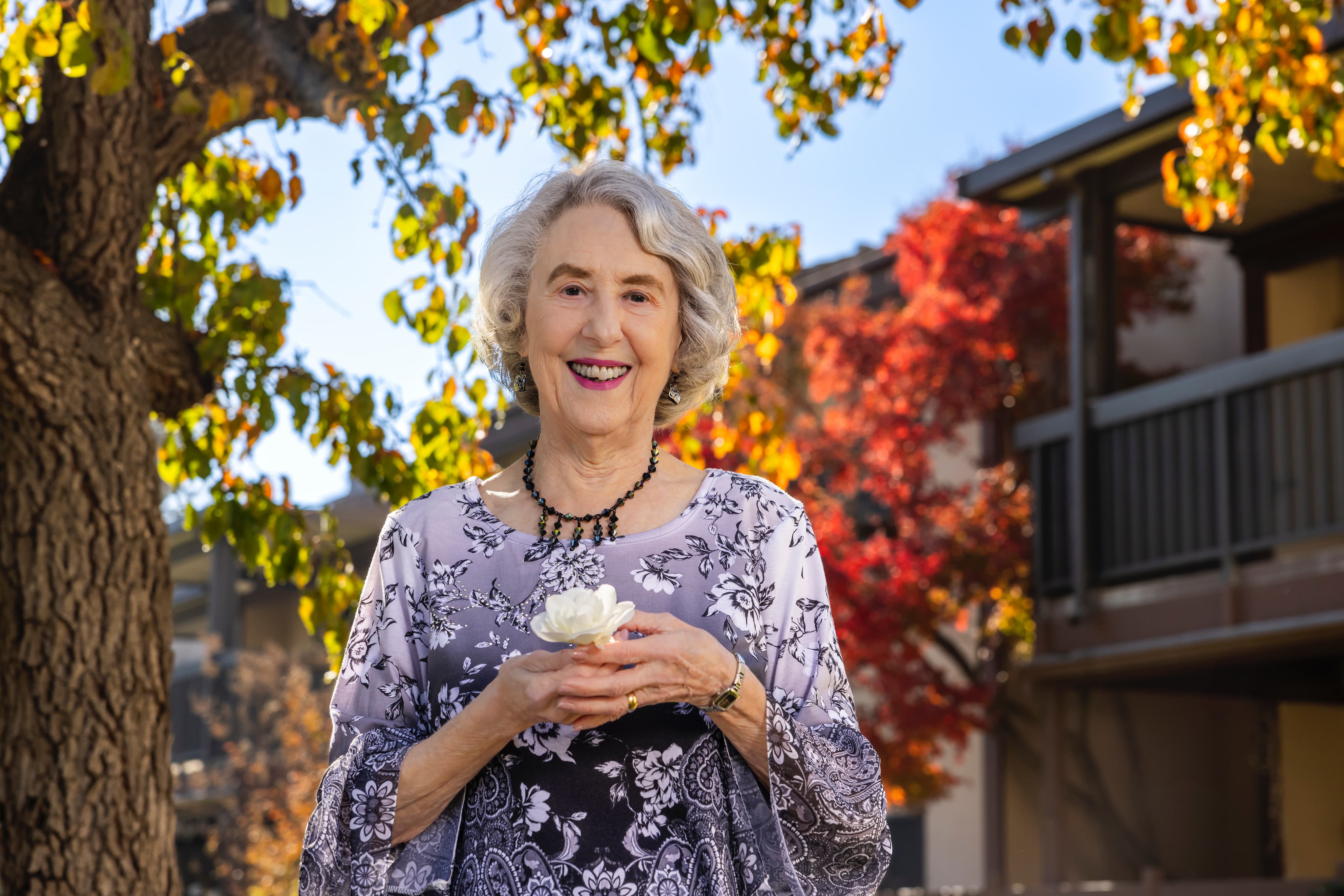Portrait of Rosewood resident Donna, standing outside and holding a white flower.