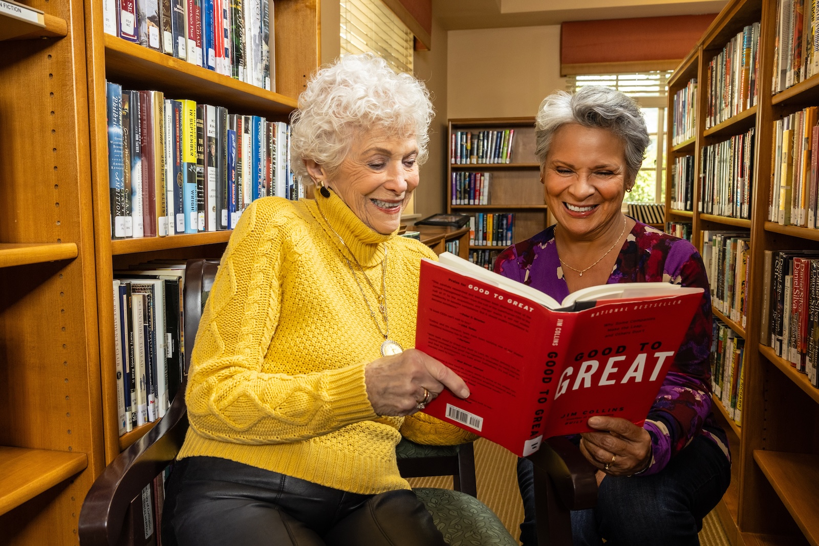 Two senior women reading a book at the library