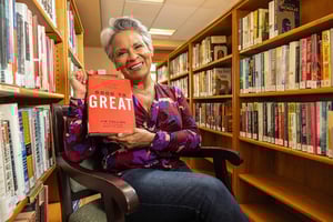 Senior woman holding up a book in the library at The Terraces of Los Gatos