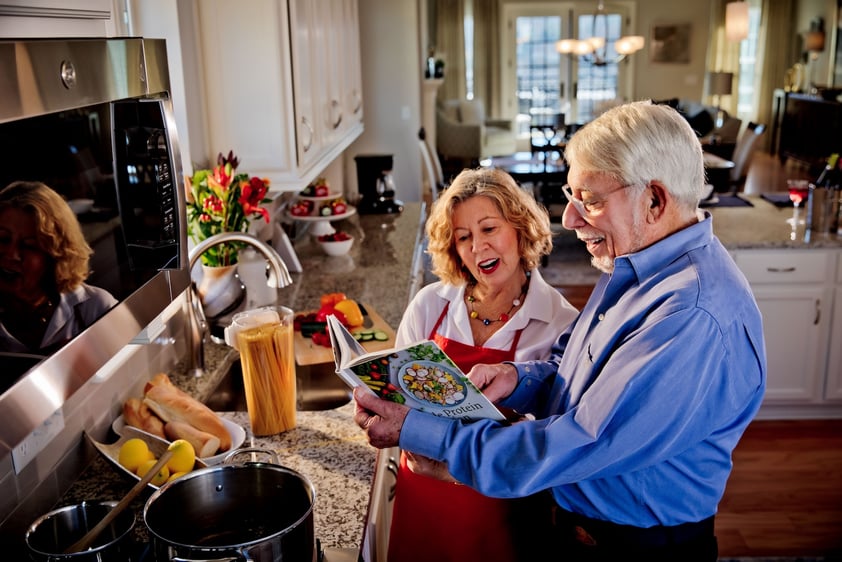 Senior couple cooking in kitchen and looking at cookbook
