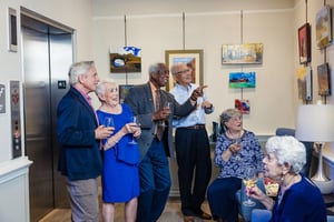 Group of seniors holding wine glasses and looking at art at an art exhibition