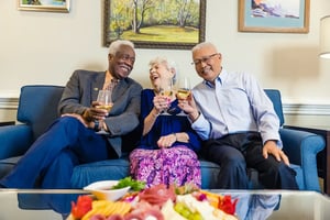 Two senior men and a senior woman sitting on a couch drinking wine