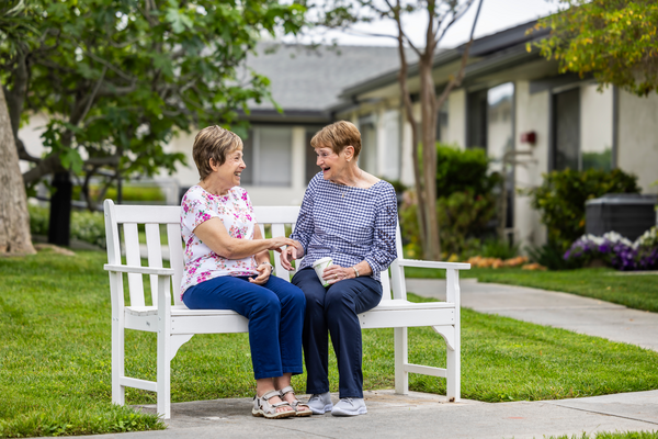 Two senior women sitting and talking on an outdoor bench on the campus of Redwood Terrace
