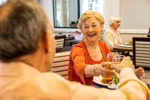 Senior couple clinking glasses of wine in the main dining room of The Terraces of Los Gatos